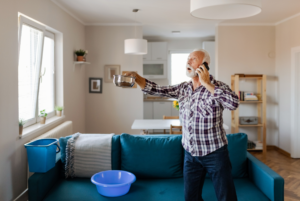 A man holding a pot and talking to someone on the phone as he tries to detect the source of a water leak