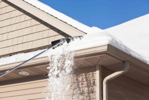 A picture of someone removing snow from their roof and tending to it as properly outlined in the article Preparing Your Roof for Winter: Top Tips for Long-Term Durability