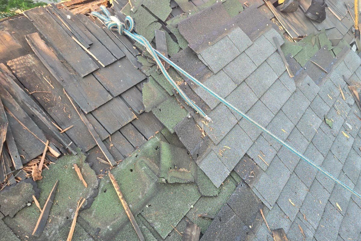 Brittle, damaged asphalt shingles being removed from a roof